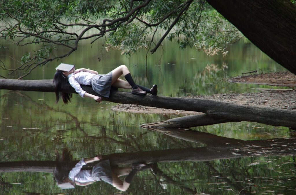 pexels-photo-267684 A young woman with a book on her face lies relaxing on a tree trunk by a tranquil lake.